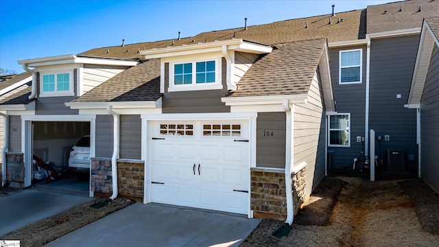 view of front of home with roof with shingles, central AC unit, a garage, stone siding, and driveway