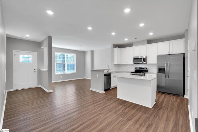 kitchen with dark wood-style floors, appliances with stainless steel finishes, open floor plan, white cabinets, and a sink