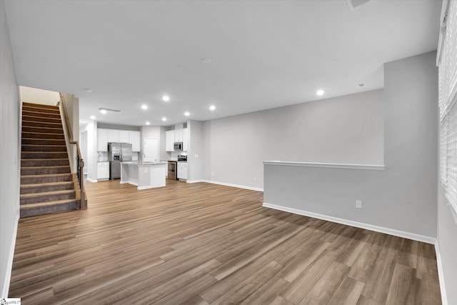 unfurnished living room featuring light wood-type flooring, stairway, baseboards, and recessed lighting