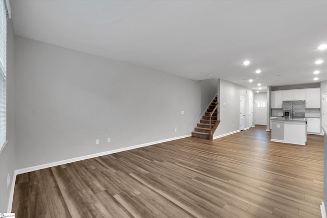 unfurnished living room featuring stairs, baseboards, wood finished floors, and recessed lighting