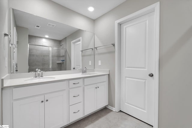 bathroom with double vanity, a shower stall, visible vents, and a sink