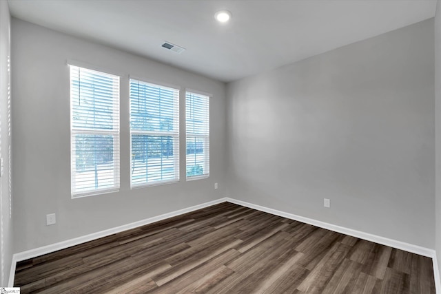 empty room featuring dark wood-style flooring, visible vents, and baseboards