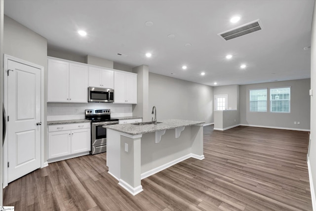 kitchen with stainless steel appliances, wood finished floors, a sink, visible vents, and an island with sink