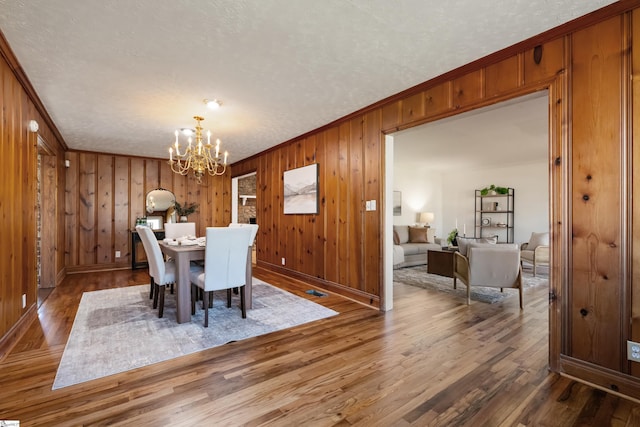 dining space with ornamental molding, wood finished floors, a textured ceiling, wood walls, and a chandelier