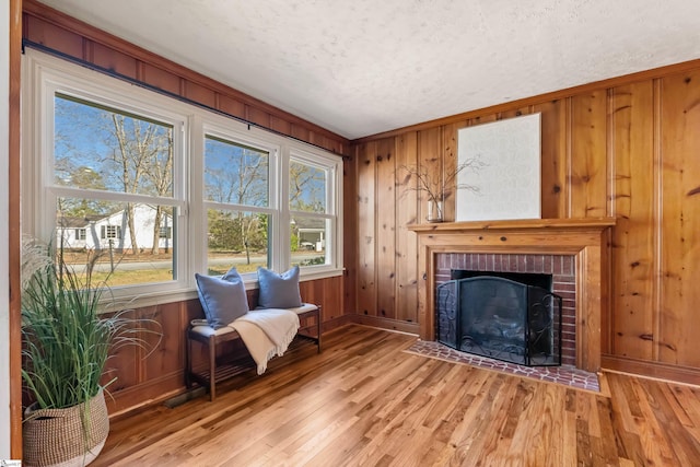 sitting room featuring wooden walls, a fireplace, a textured ceiling, and wood finished floors