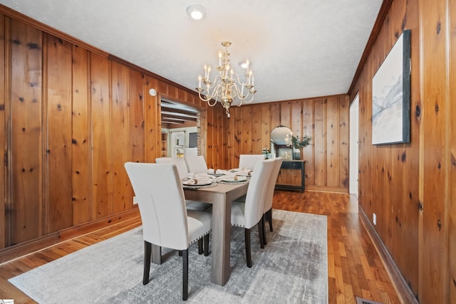 dining space featuring an inviting chandelier, baseboards, wood finished floors, and wood walls