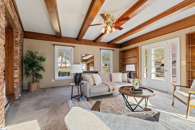 living area featuring carpet floors, wood walls, beamed ceiling, and a ceiling fan