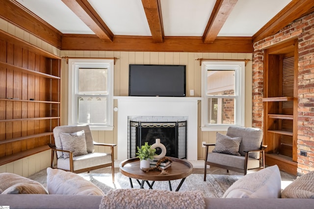 living room with a wealth of natural light, a brick fireplace, beamed ceiling, and wooden walls