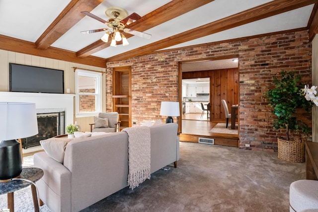 living area featuring visible vents, a ceiling fan, beamed ceiling, carpet, and a fireplace