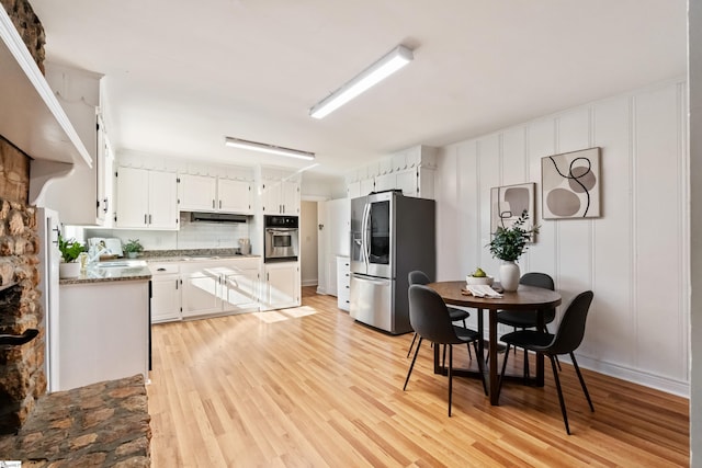 kitchen with stainless steel appliances, white cabinets, light wood-style floors, and under cabinet range hood