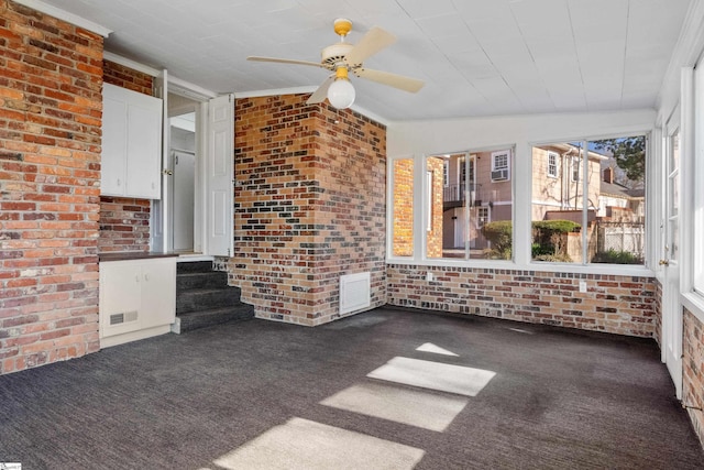 interior space with lofted ceiling, brick wall, carpet floors, visible vents, and a ceiling fan