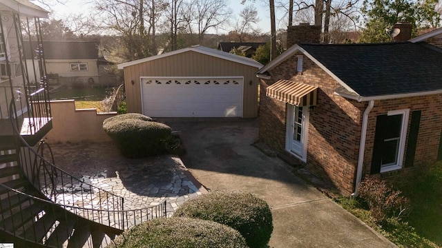 view of property exterior featuring a garage, a chimney, roof with shingles, an outdoor structure, and brick siding