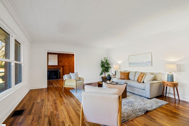 living room with a brick fireplace, wood finished floors, visible vents, and baseboards