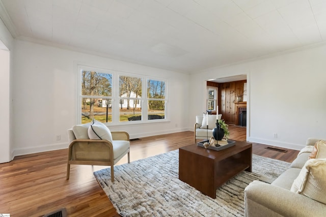 living area with baseboards, visible vents, wood finished floors, crown molding, and a fireplace