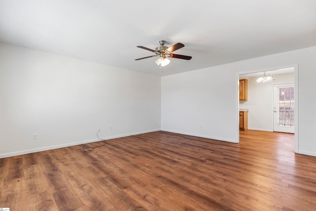 empty room featuring baseboards, wood finished floors, and ceiling fan with notable chandelier