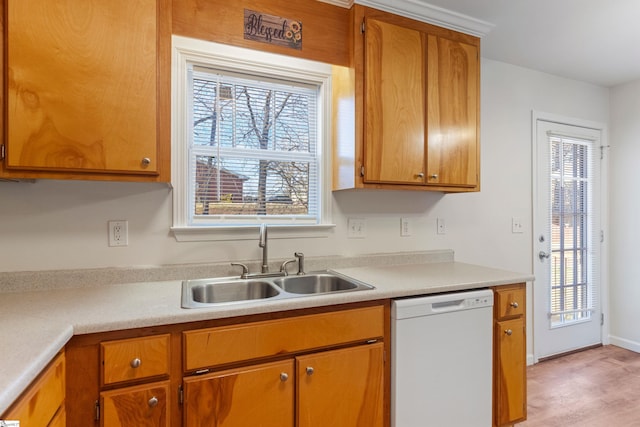 kitchen with light countertops, brown cabinetry, white dishwasher, and a sink