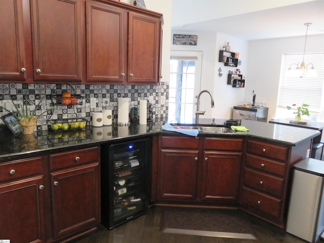 kitchen featuring beverage cooler, a peninsula, a sink, backsplash, and dark stone counters