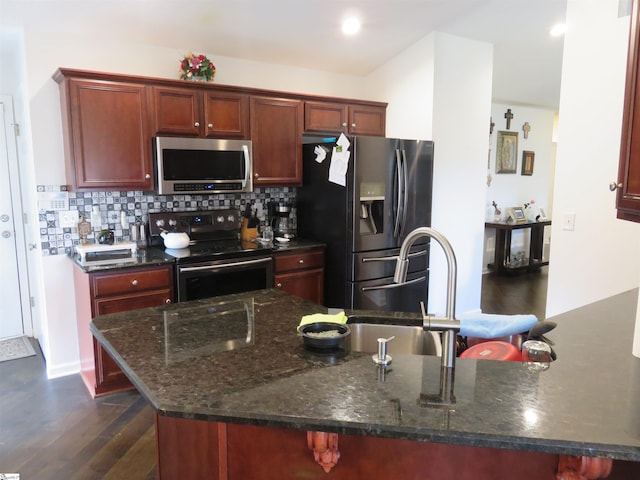 kitchen with reddish brown cabinets, dark wood finished floors, decorative backsplash, dark stone countertops, and stainless steel appliances