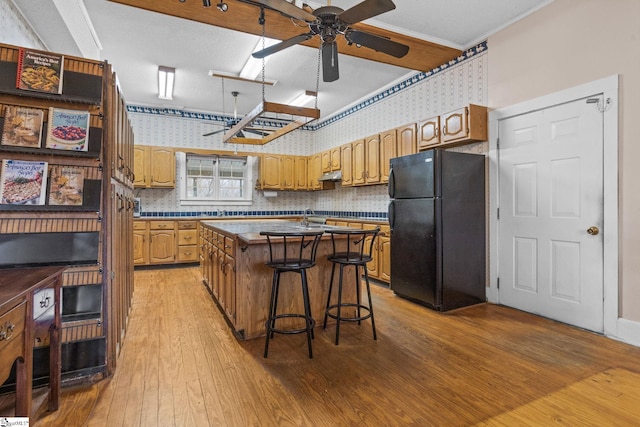 kitchen with dark countertops, light wood-style floors, freestanding refrigerator, a kitchen island, and wallpapered walls