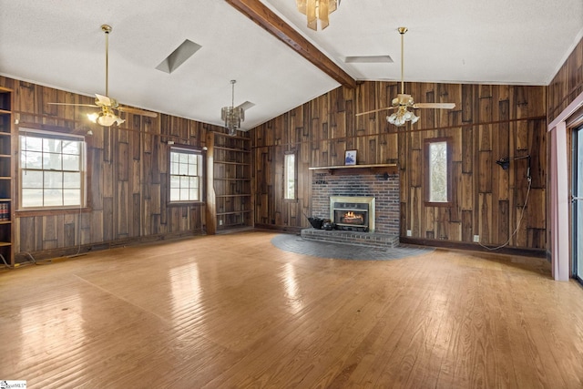 unfurnished living room with lofted ceiling with beams, wooden walls, a fireplace, wood finished floors, and a ceiling fan