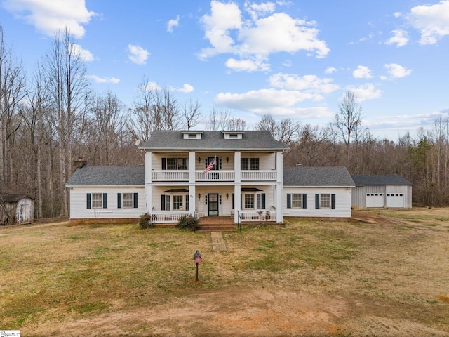 greek revival inspired property with a balcony, a storage unit, an outdoor structure, a porch, and a front yard