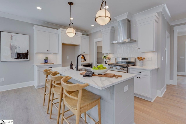 kitchen featuring gas range, wall chimney exhaust hood, white cabinetry, and a sink