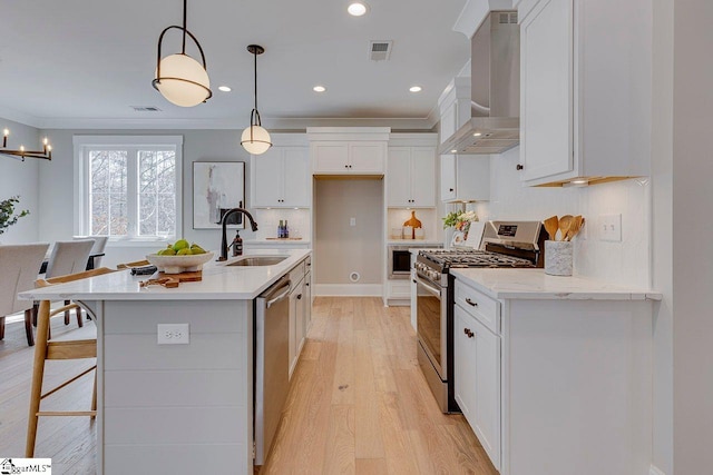 kitchen featuring light wood finished floors, stainless steel appliances, white cabinetry, a sink, and wall chimney range hood