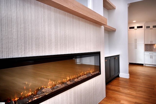 interior space with recessed lighting, backsplash, a glass covered fireplace, wood finished floors, and baseboards