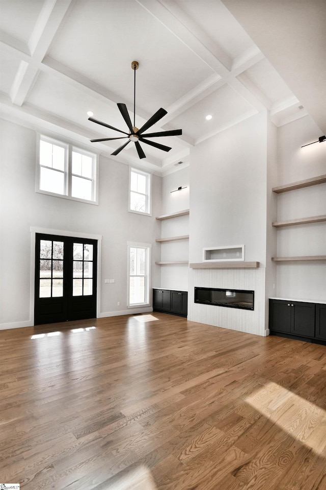 unfurnished living room featuring built in features, french doors, a glass covered fireplace, wood finished floors, and baseboards