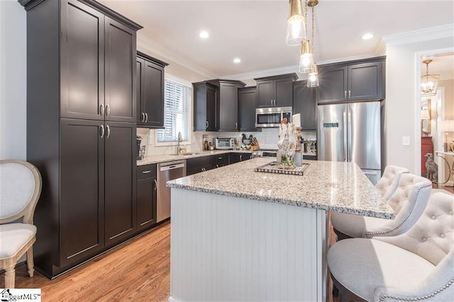 kitchen with a kitchen island, appliances with stainless steel finishes, a breakfast bar, ornamental molding, and a sink