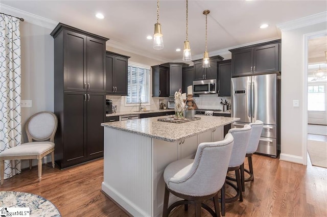 kitchen with appliances with stainless steel finishes, wood finished floors, a center island, crown molding, and a sink