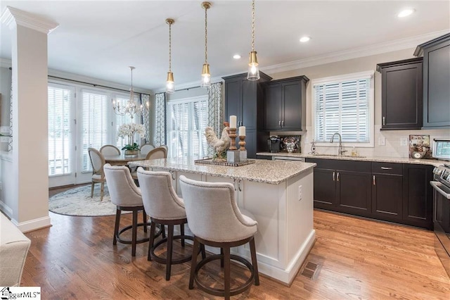 kitchen with light stone counters, crown molding, a breakfast bar area, a kitchen island, and a sink