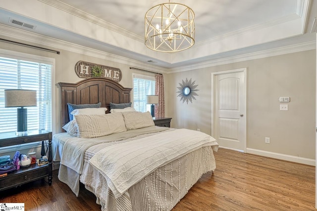 bedroom featuring a tray ceiling, visible vents, an inviting chandelier, and wood finished floors