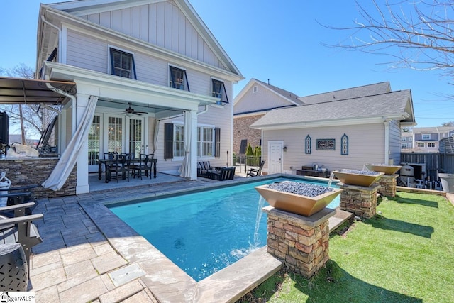 back of property with a fenced in pool, ceiling fan, fence, a patio area, and board and batten siding