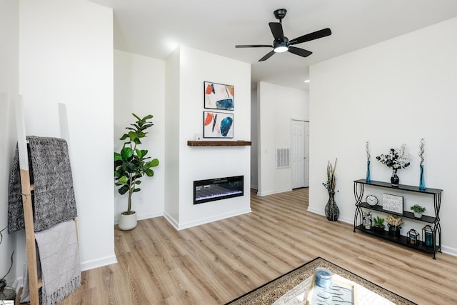 living area with visible vents, baseboards, a glass covered fireplace, light wood-style flooring, and ceiling fan