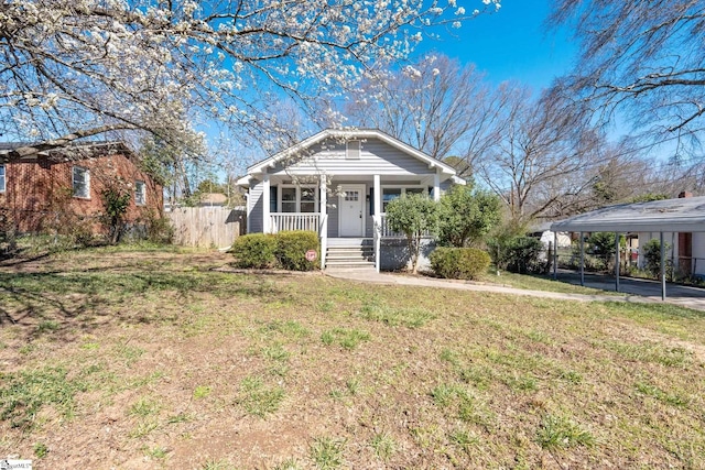 view of front facade featuring fence, a front lawn, a porch, and a detached carport