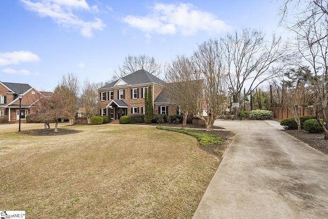 view of front facade featuring a front yard, concrete driveway, brick siding, and fence