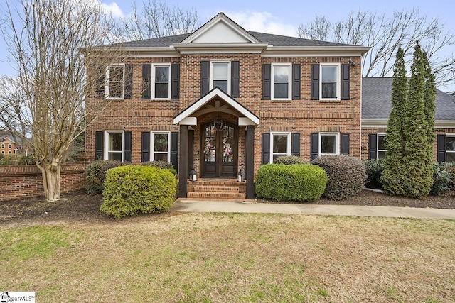 view of front of home with roof with shingles, brick siding, and a front lawn