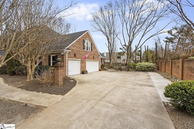 view of side of property with a garage, concrete driveway, brick siding, and fence