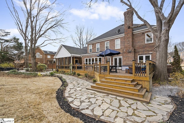 rear view of house featuring a sunroom, a wooden deck, a chimney, and brick siding