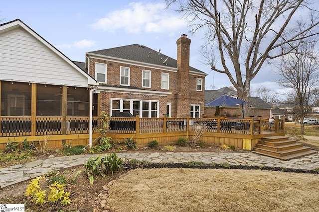 back of property featuring a sunroom, a chimney, a deck, and brick siding