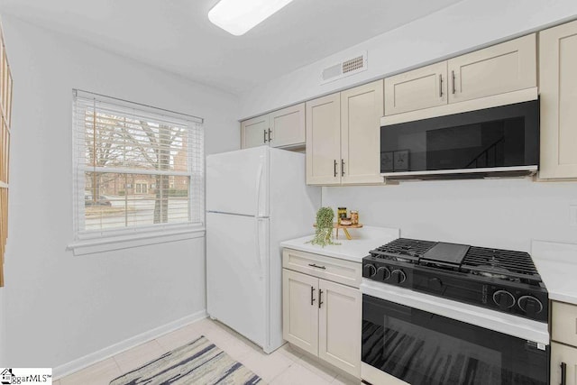 kitchen with gas range oven, light countertops, visible vents, freestanding refrigerator, and baseboards