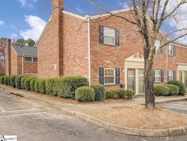 view of property featuring a chimney and brick siding