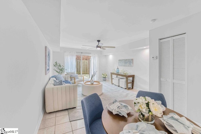 living area with light tile patterned floors, a ceiling fan, and baseboards