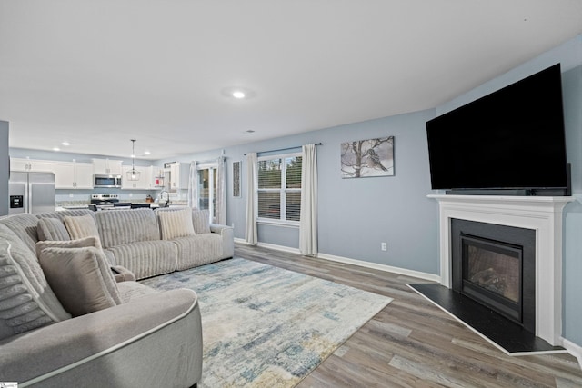 living room featuring light wood finished floors, recessed lighting, baseboards, and a glass covered fireplace