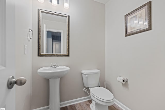 half bathroom featuring baseboards, a sink, toilet, and wood finished floors