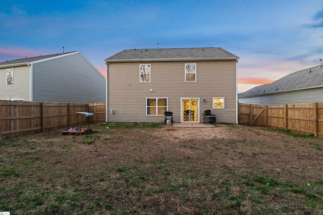 back of property at dusk with a patio area, a fenced backyard, and a lawn