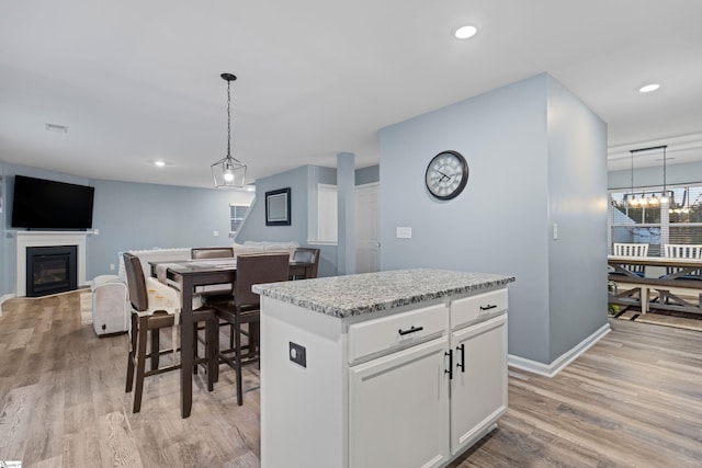 kitchen with hanging light fixtures, light wood finished floors, a glass covered fireplace, and white cabinetry