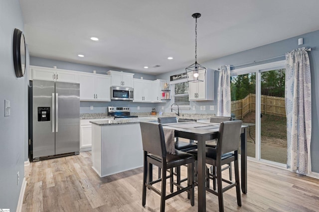 kitchen with pendant lighting, stainless steel appliances, light wood-type flooring, and white cabinets