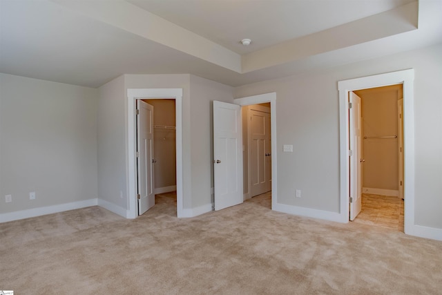 unfurnished bedroom featuring baseboards, a tray ceiling, a walk in closet, carpet flooring, and a closet